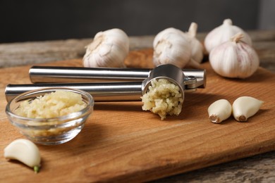 Garlic press, cloves and mince on wooden table, closeup