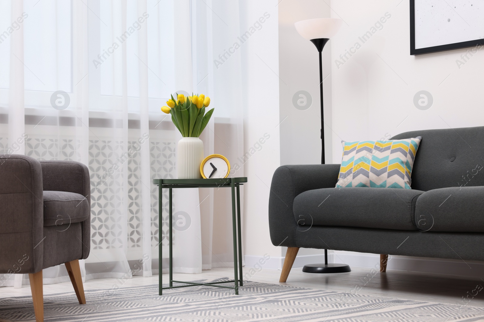 Photo of Spring atmosphere. Stylish living room interior with comfortable furniture and bouquet of beautiful yellow tulips