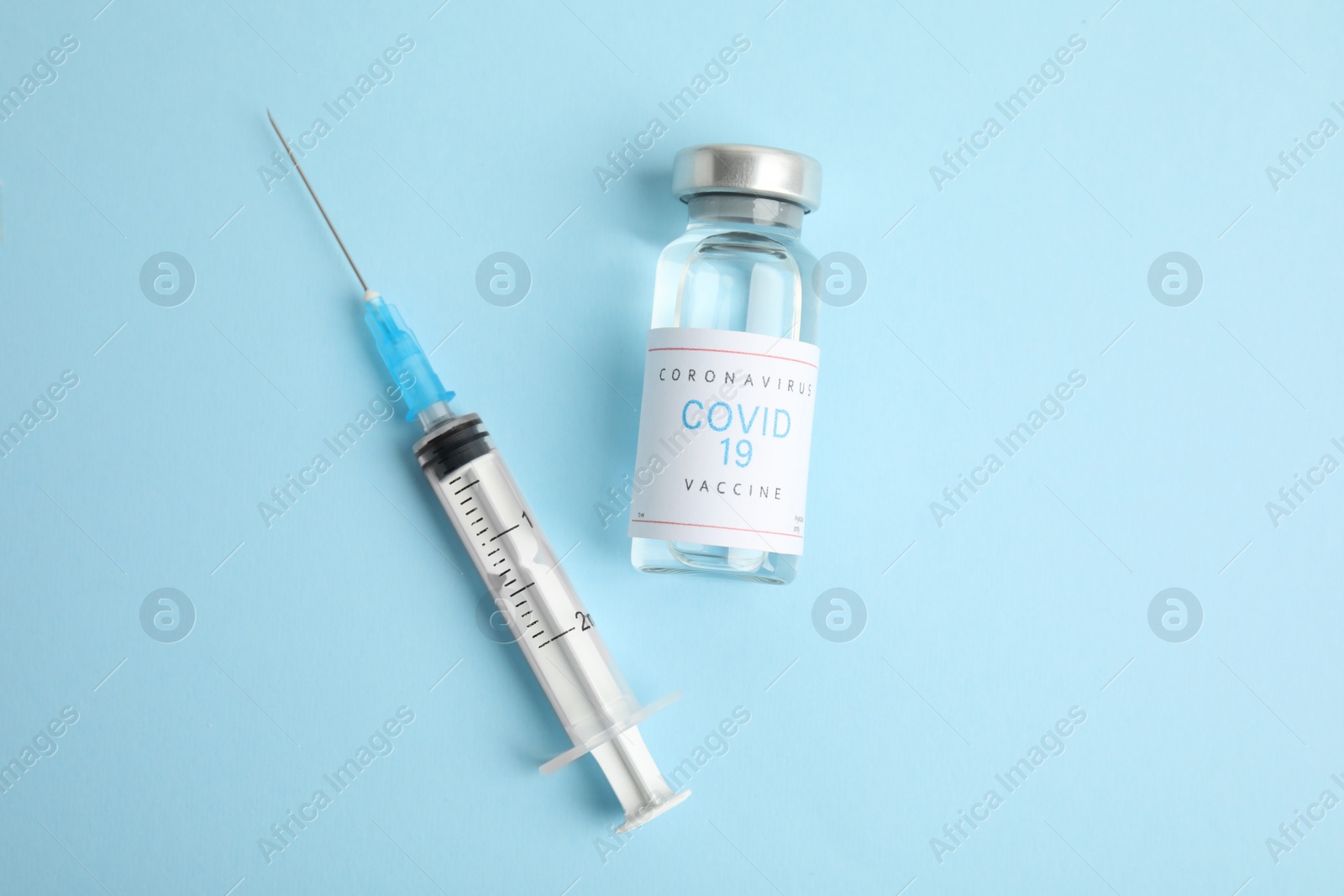 Photo of Vial with coronavirus vaccine and syringe on light blue background, flat lay