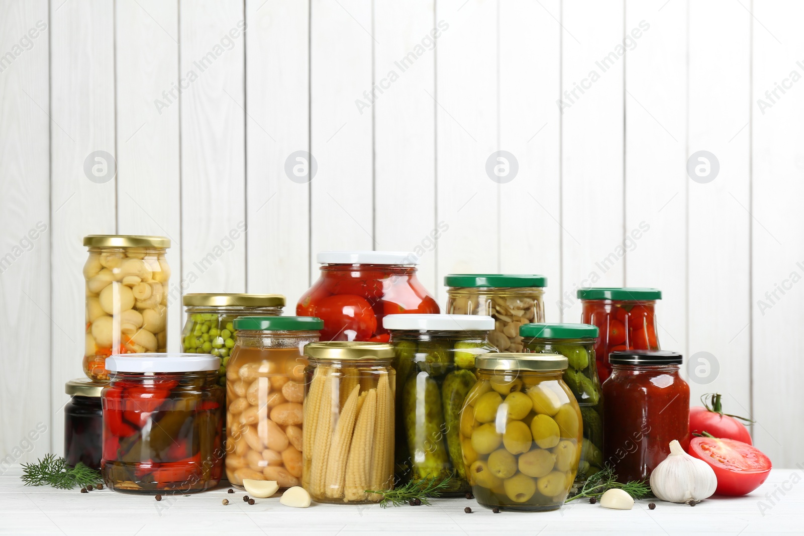 Photo of Glass jars with different pickled vegetables and mushrooms on white wooden background