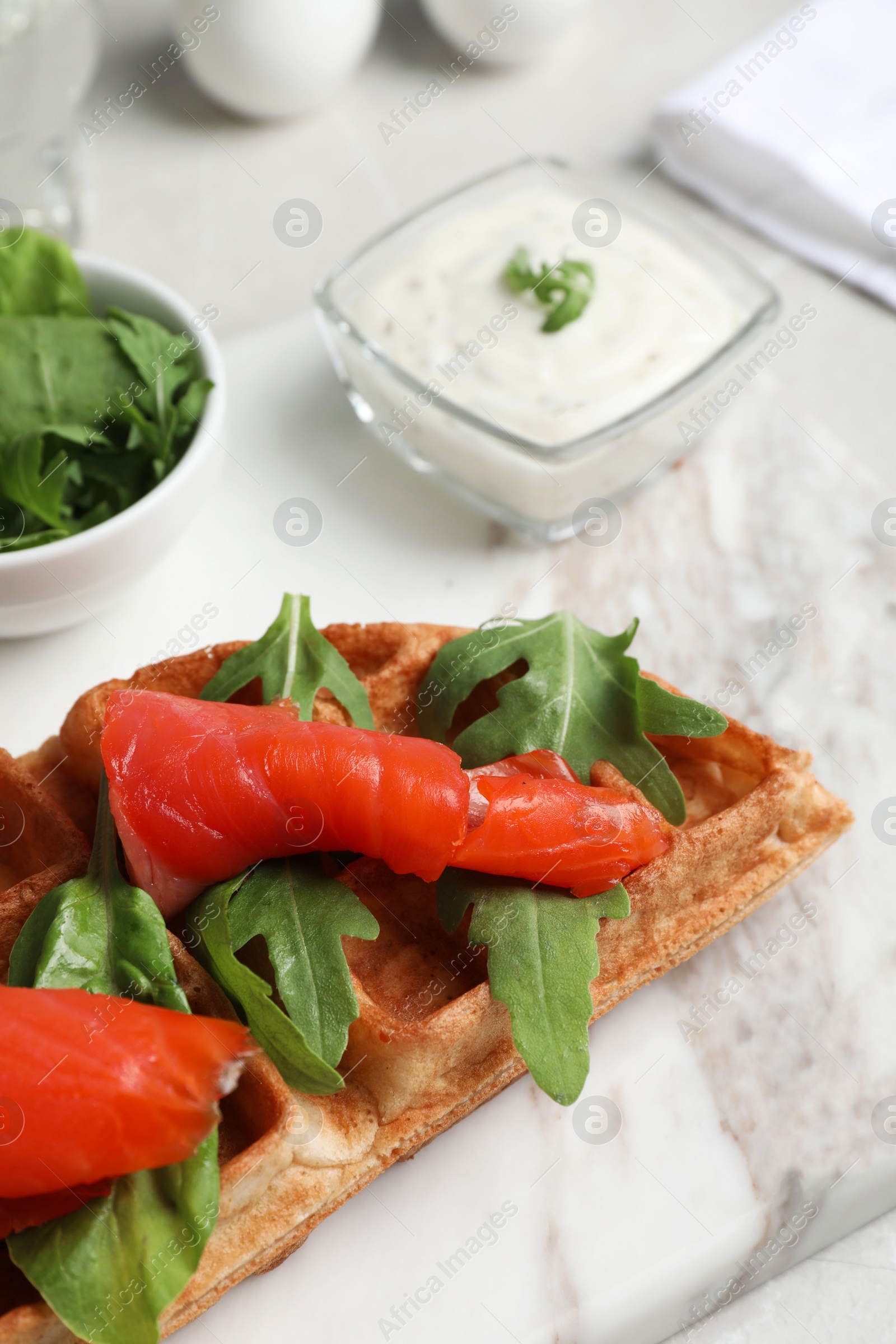 Photo of Fresh Belgian waffle with salmon and arugula on white table, closeup