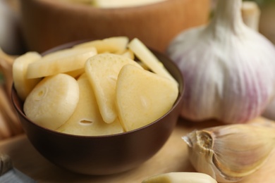Photo of Fresh sliced garlic cloves in bowl on wooden table, closeup. Organic product