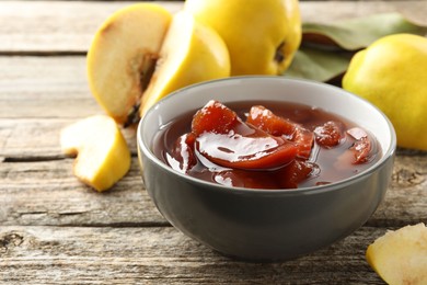 Photo of Tasty homemade quince jam in bowl and fruits on wooden table, closeup