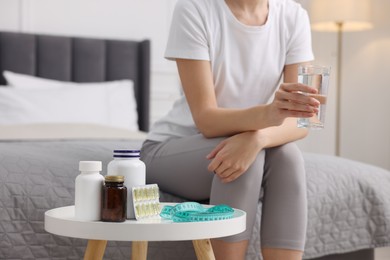 Woman holding glass of water near table with pills and measuring tape in room, closeup. Weight loss