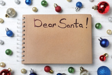 Photo of Notebook with words DEAR SANTA and Christmas decorations on white wooden table, flat lay. Space for text