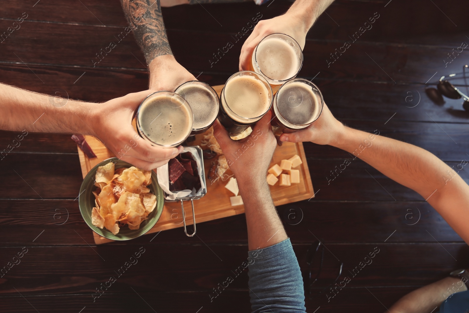 Photo of Friends clinking glasses with beer at table, top view