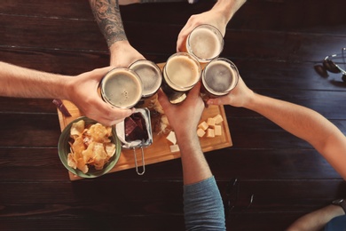 Photo of Friends clinking glasses with beer at table, top view