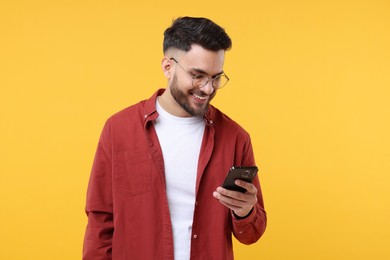 Happy young man using smartphone on yellow background