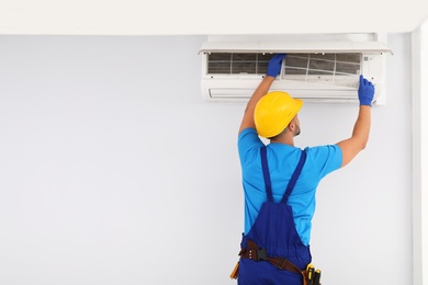 Photo of Professional technician maintaining modern air conditioner indoors. Space for text