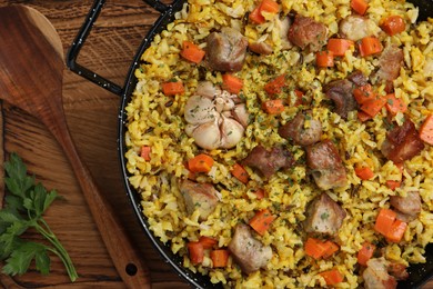 Delicious pilaf with meat, carrot and garlic served on wooden table, flat lay