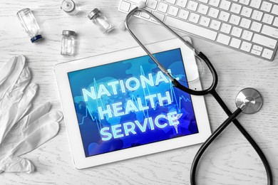 National health service (NHS). Tablet with text, stethoscope, drugs, gloves and keyboard on white wooden background, flat lay