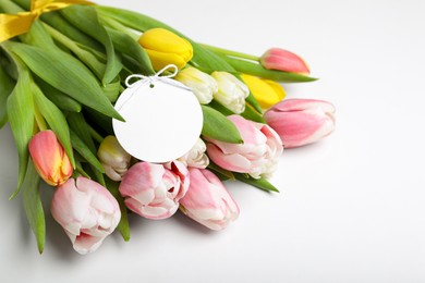 Bouquet of beautiful tulips and blank card on light background, closeup. Birthday celebration