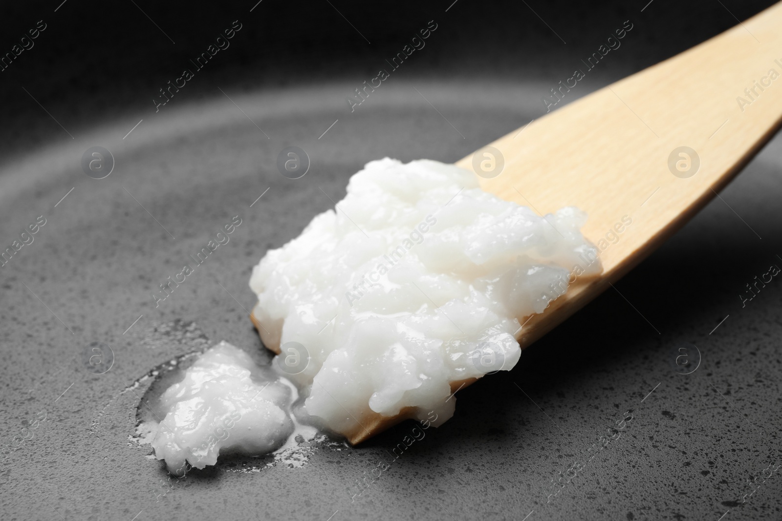 Photo of Frying pan with coconut oil and wooden spatula, closeup. Healthy cooking