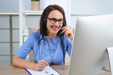 Doctor with headset and computer consulting patient online in office. Hotline service