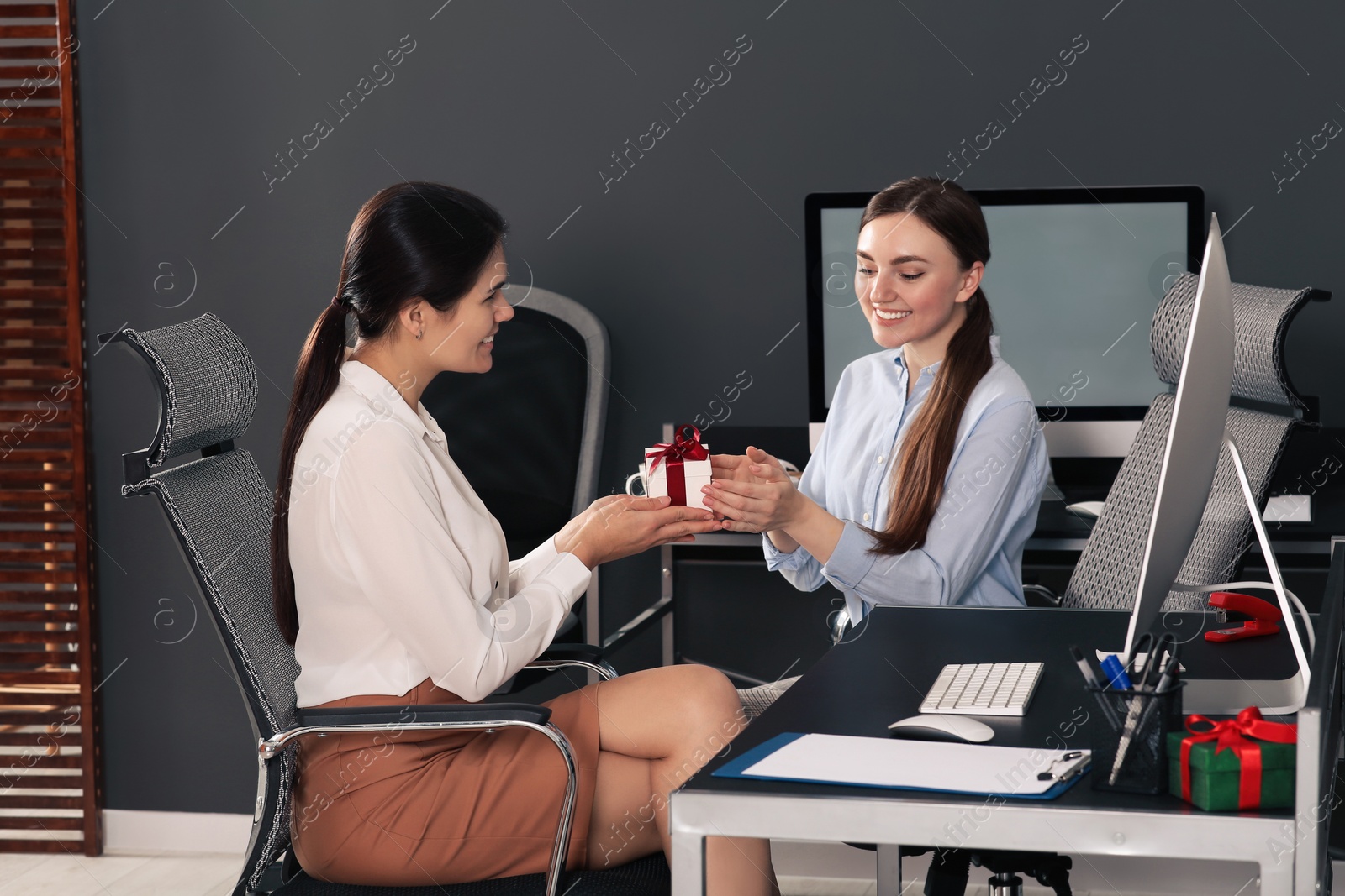 Photo of Woman presenting gift to her colleague in office