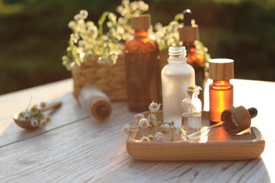Photo of Chamomile essential oil, pipette and flowers on white wooden table outdoors, space for text