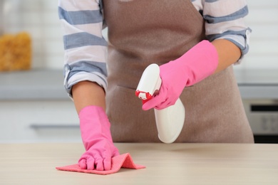 Photo of Woman cleaning table with rag in kitchen, closeup