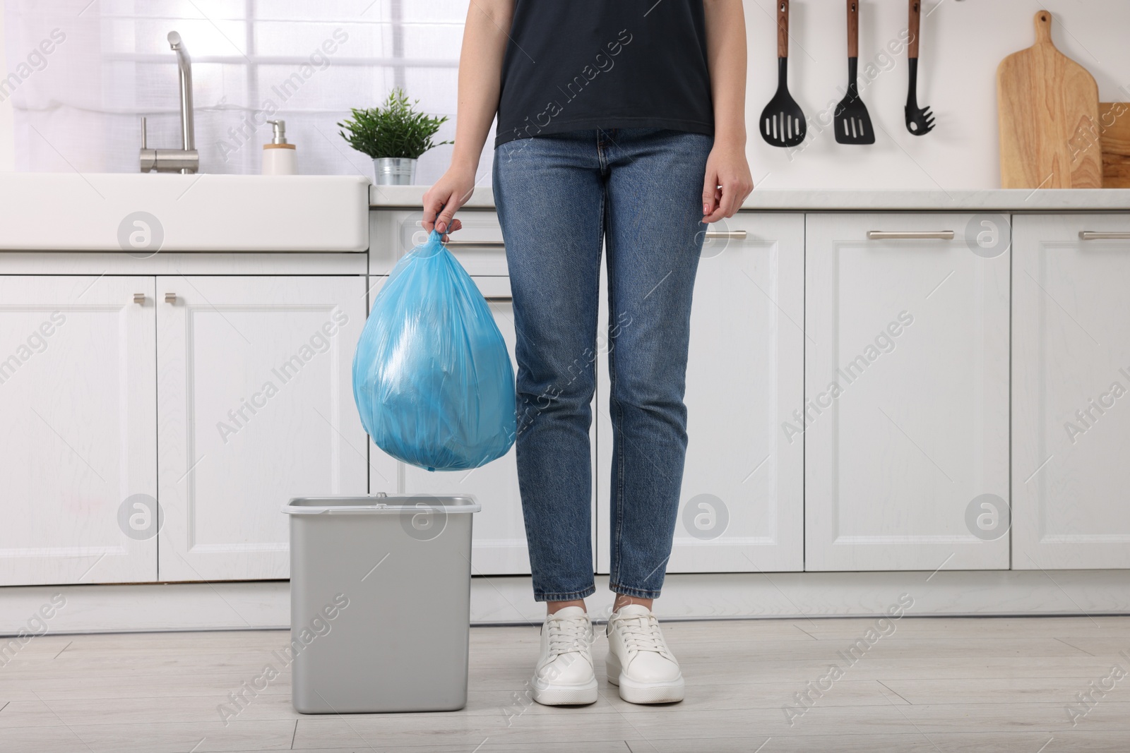 Photo of Woman taking garbage bag out of trash bin in kitchen, closeup