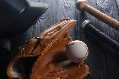 Baseball glove, bats, ball and batting helmet on black wooden table, closeup