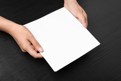 Photo of Woman holding blank paper sheets for brochure at black wooden table. Mock up