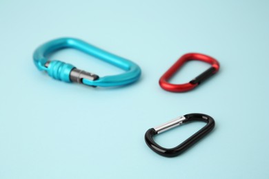 Photo of Metal carabiners on light blue background, closeup