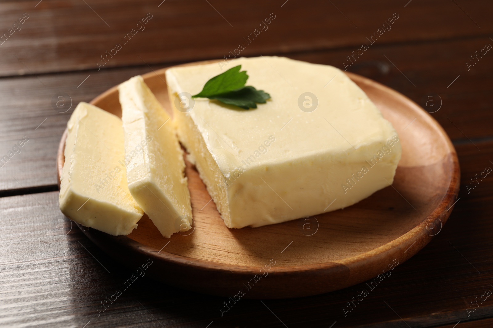 Photo of Cut tasty butter with parsley on wooden table