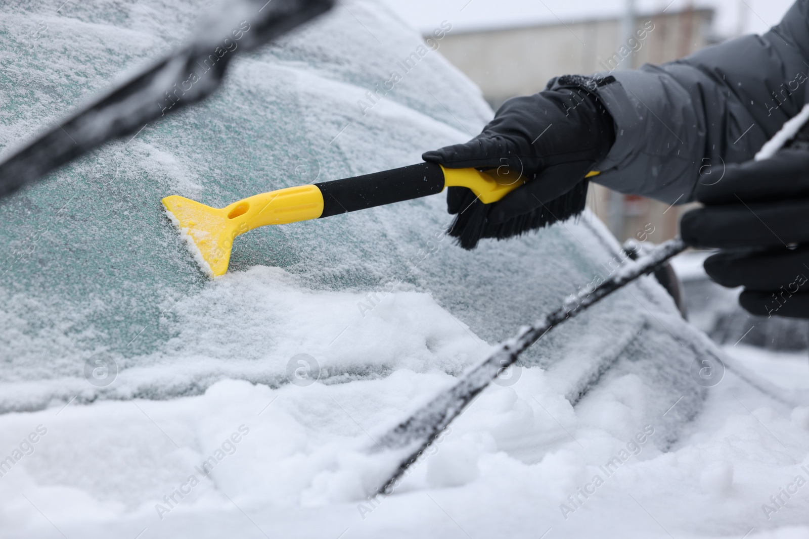 Photo of Man cleaning snow from car windshield outdoors, closeup