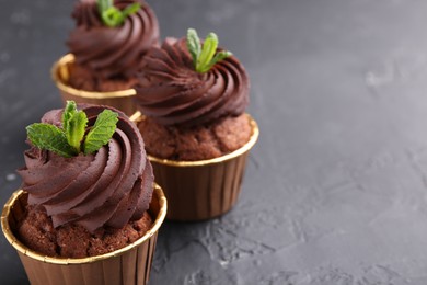 Photo of Delicious chocolate cupcakes with mint on black textured table, closeup. Space for text