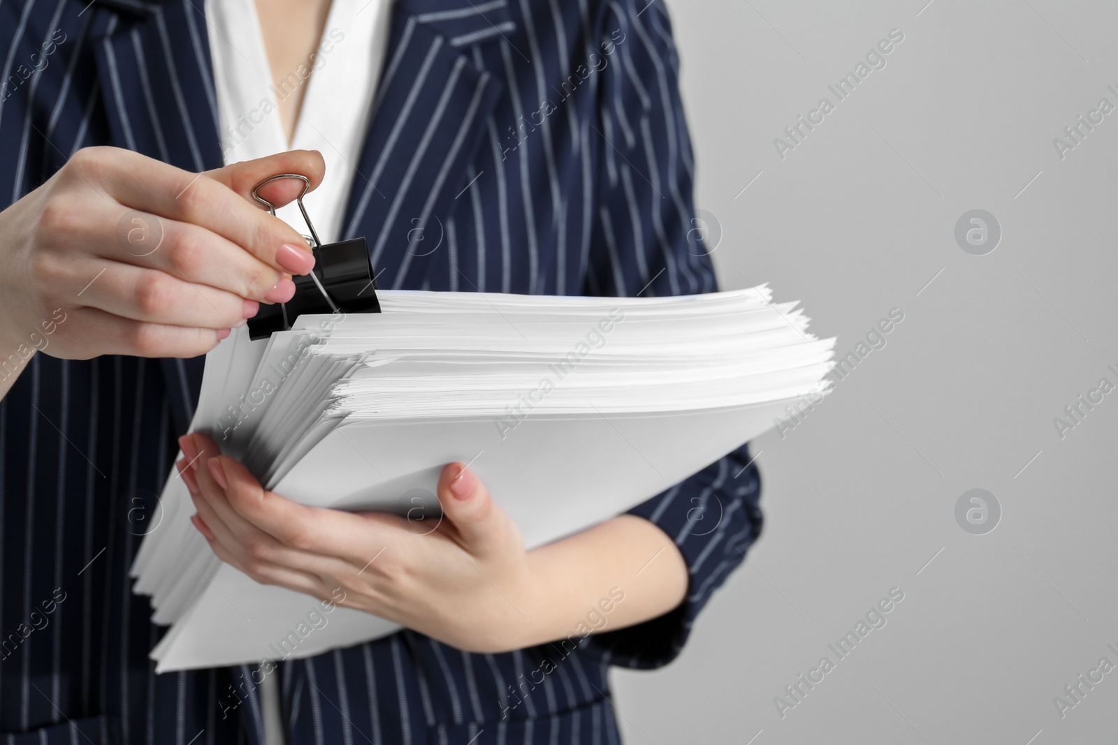 Photo of Woman attaching documents with metal binder clip on grey background, closeup