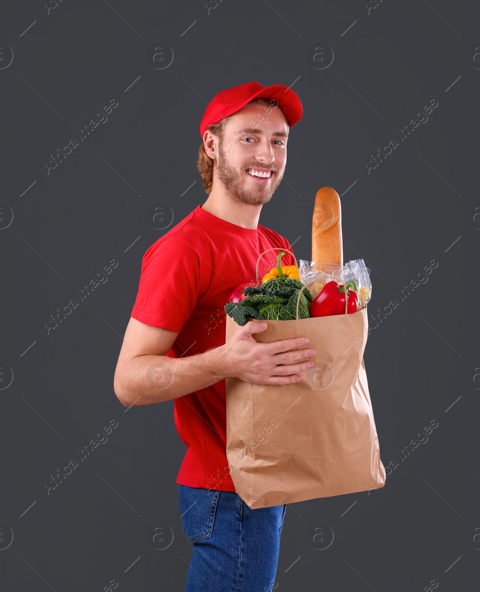 Photo of Delivery man holding paper bag with food products on dark background