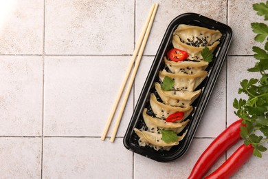 Photo of Delicious gyoza (asian dumplings) with chili peppers, parsley and chopsticks on light tiled table, flat lay. Space for text