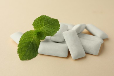 Photo of Tasty white chewing gums and mint leaves on beige background, closeup