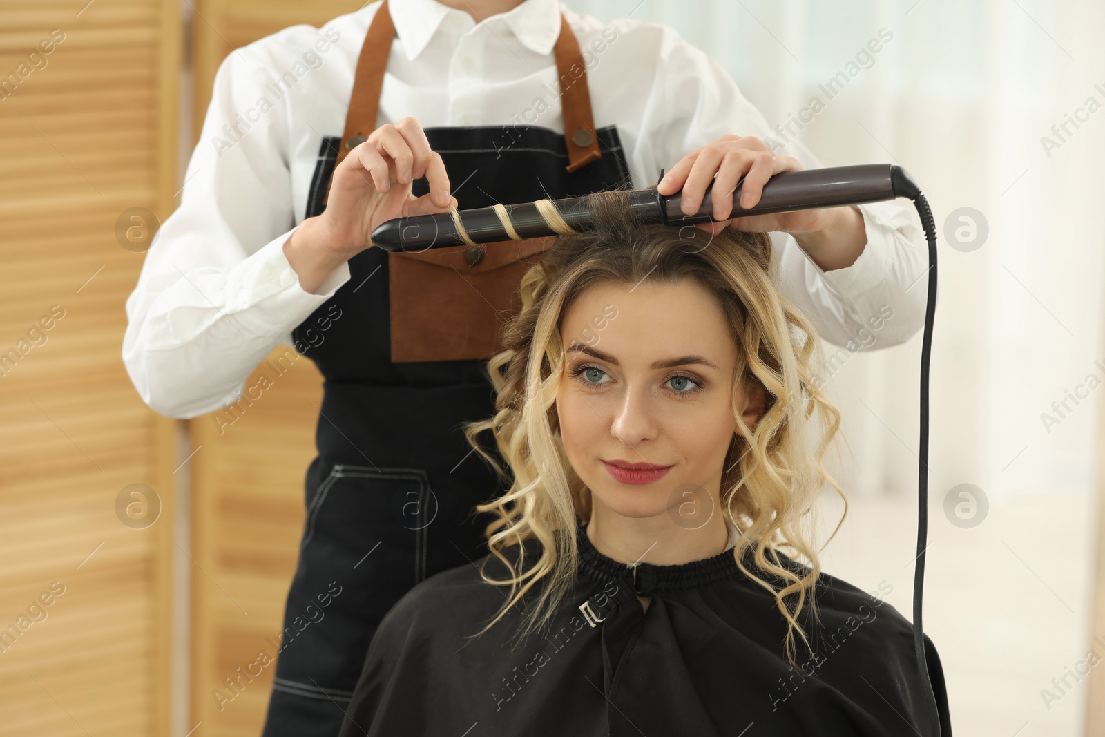 Photo of Hair styling. Hairdresser curling woman's hair in salon, closeup