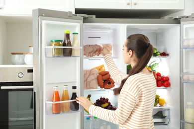 Photo of Young woman taking ham out of refrigerator in kitchen