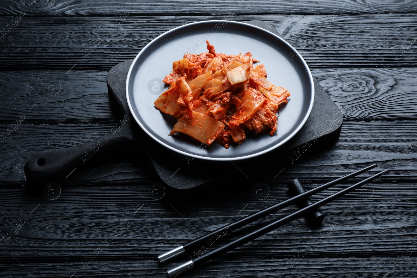 Photo of Delicious kimchi with Chinese cabbage served on black wooden table