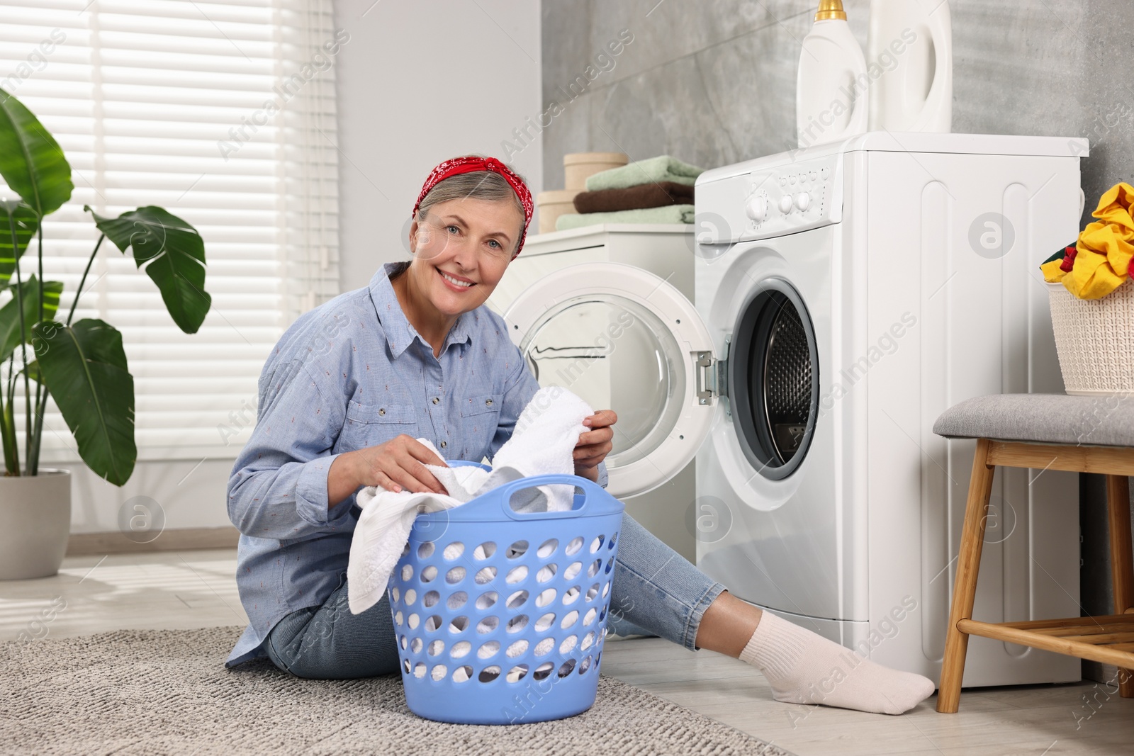 Photo of Happy housewife with laundry basket near washing machine at home