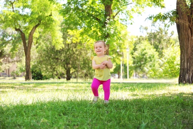 Cute baby girl learning to walk in park on sunny day