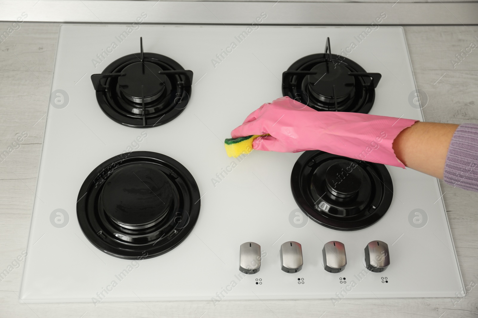 Photo of Woman cleaning gas stove with sponge, closeup