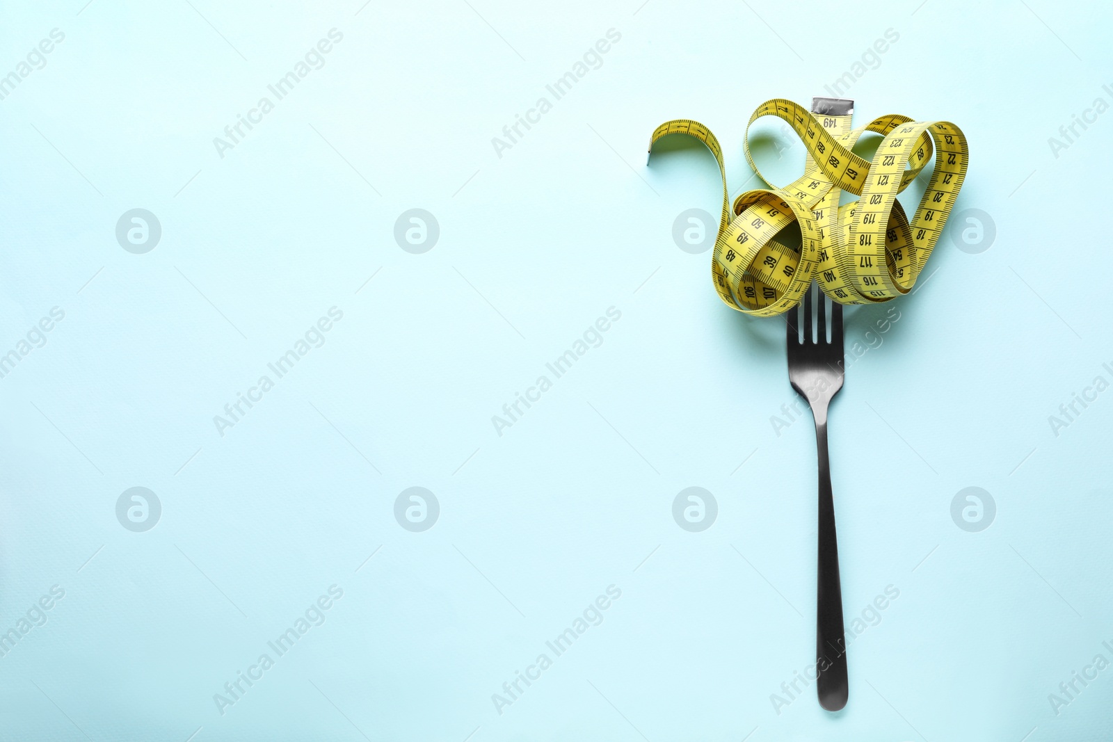 Photo of Fork with measuring tape on light blue background, top view and space for text. Diet concept