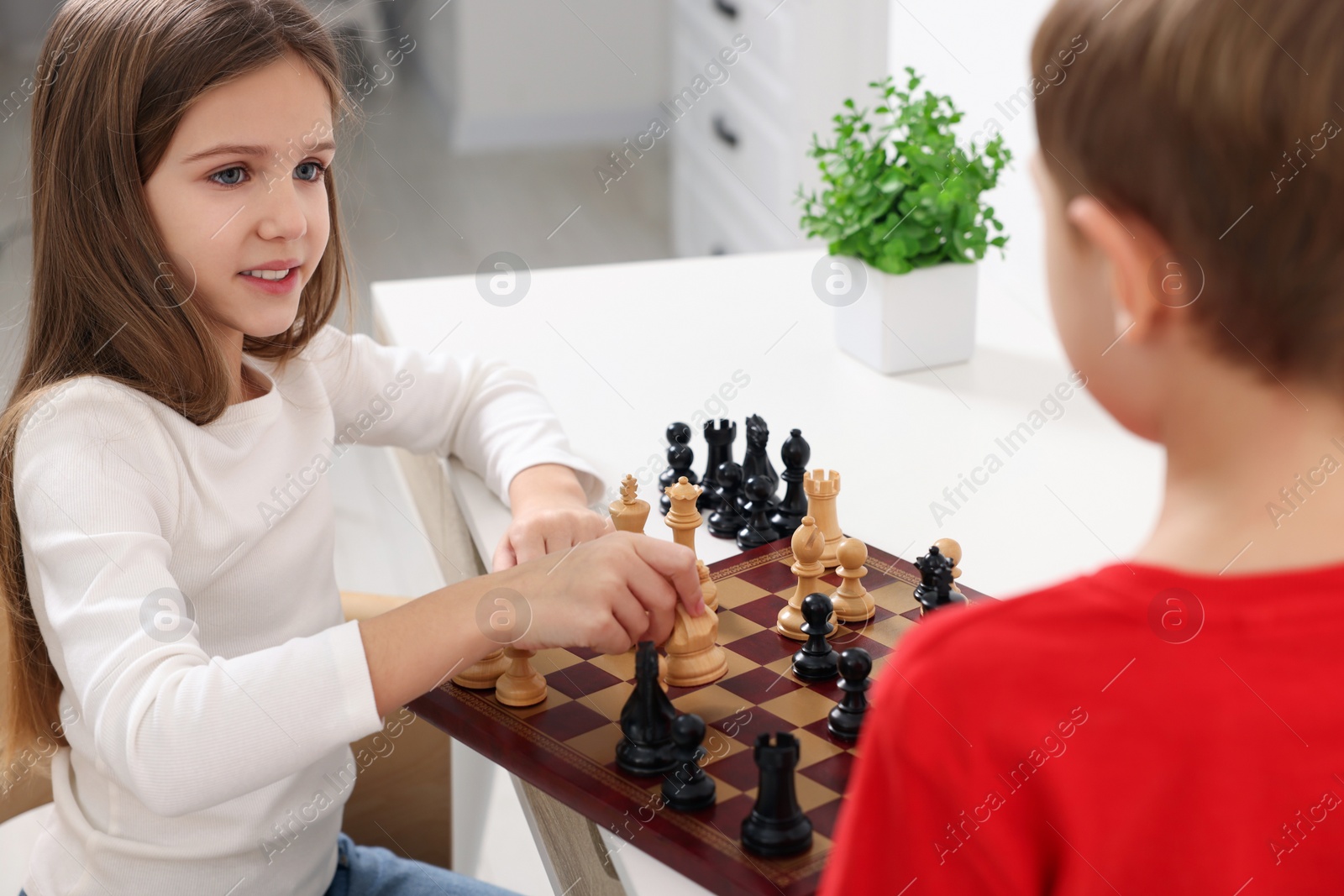 Photo of Cute children playing chess at table in room