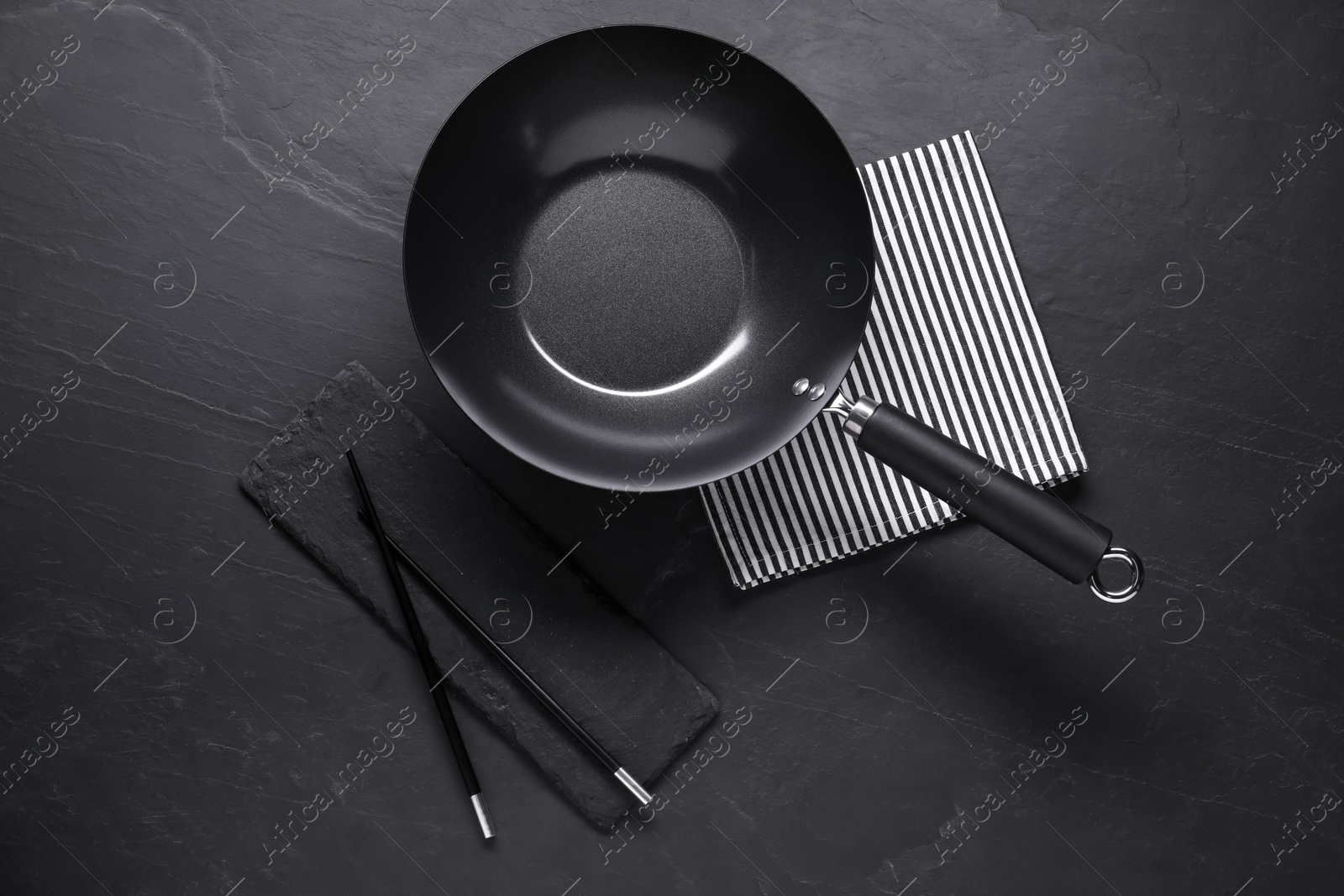 Photo of Empty iron wok and chopsticks on black table, flat lay