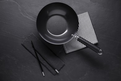 Empty iron wok and chopsticks on black table, flat lay