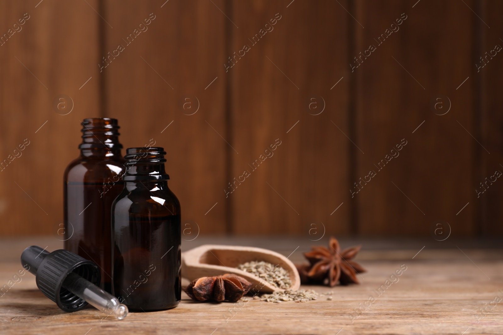 Photo of Bottles of essential oil, anise and seeds on wooden table. Space for text