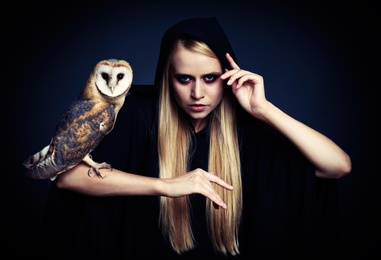 Photo of Witch in black mantle with owl on dark background. Scary fantasy character