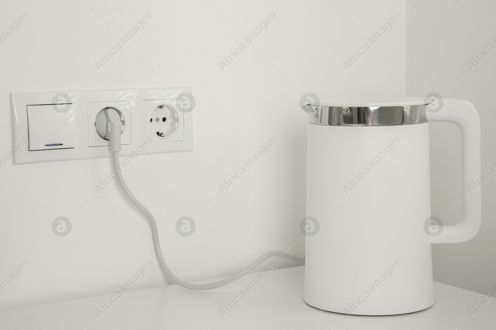 Photo of Electric kettle plugged into power socket on white wall