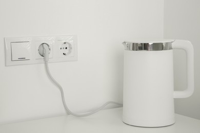 Photo of Electric kettle plugged into power socket on white wall