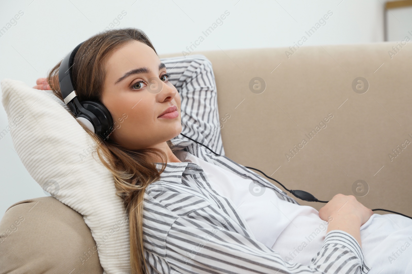 Photo of Young woman with headphones on sofa at home