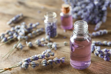 Bottle of natural essential oil and lavender flowers on wooden background