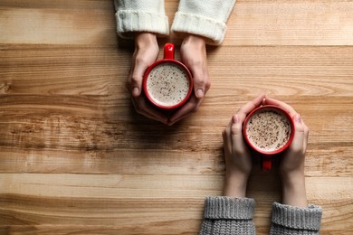 Photo of Women with cups of coffee at wooden table, top view