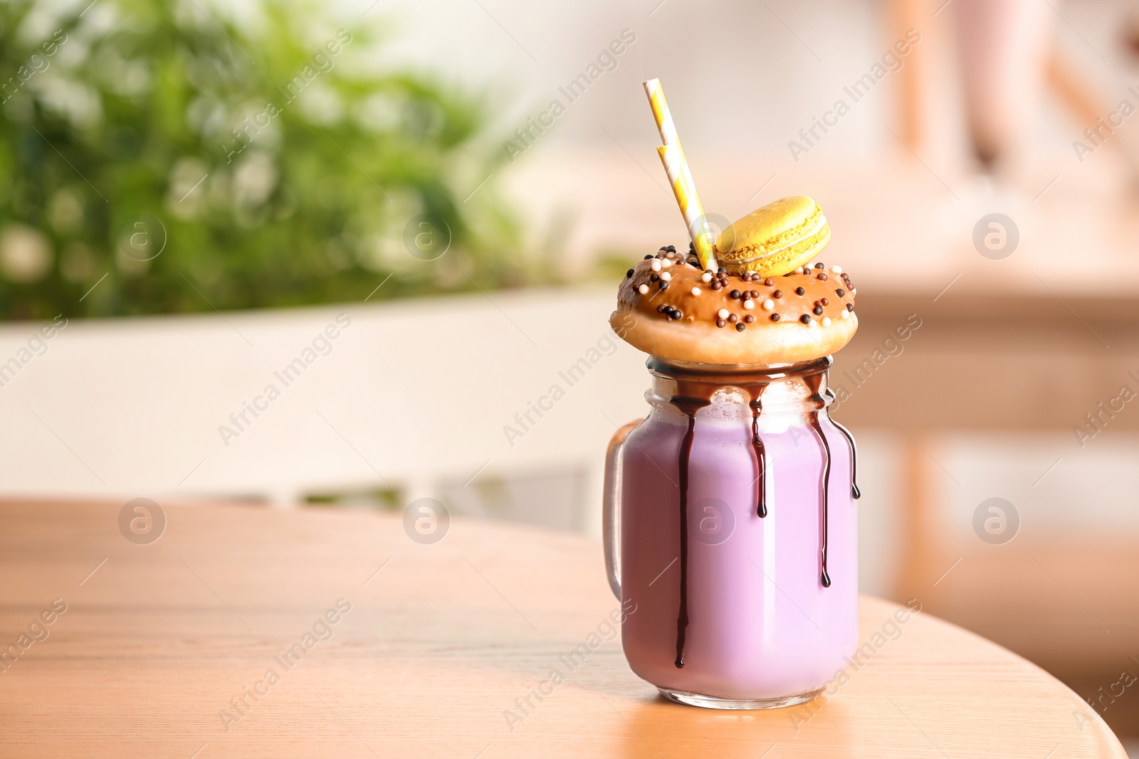 Photo of Mason jar with delicious milk shake on table against blurred background. Space for text